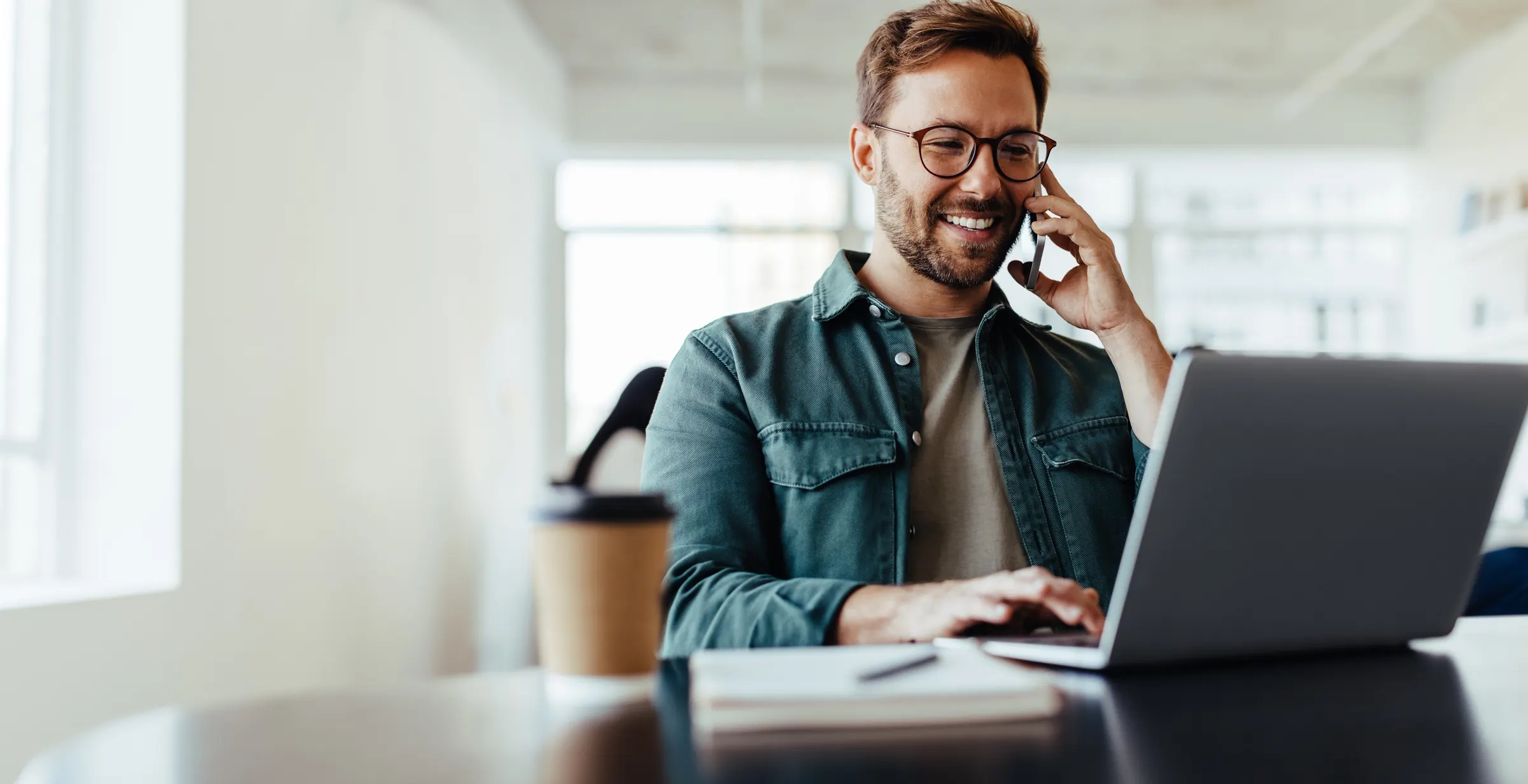 Smiling man on a phone call while working on a laptop at his desk.